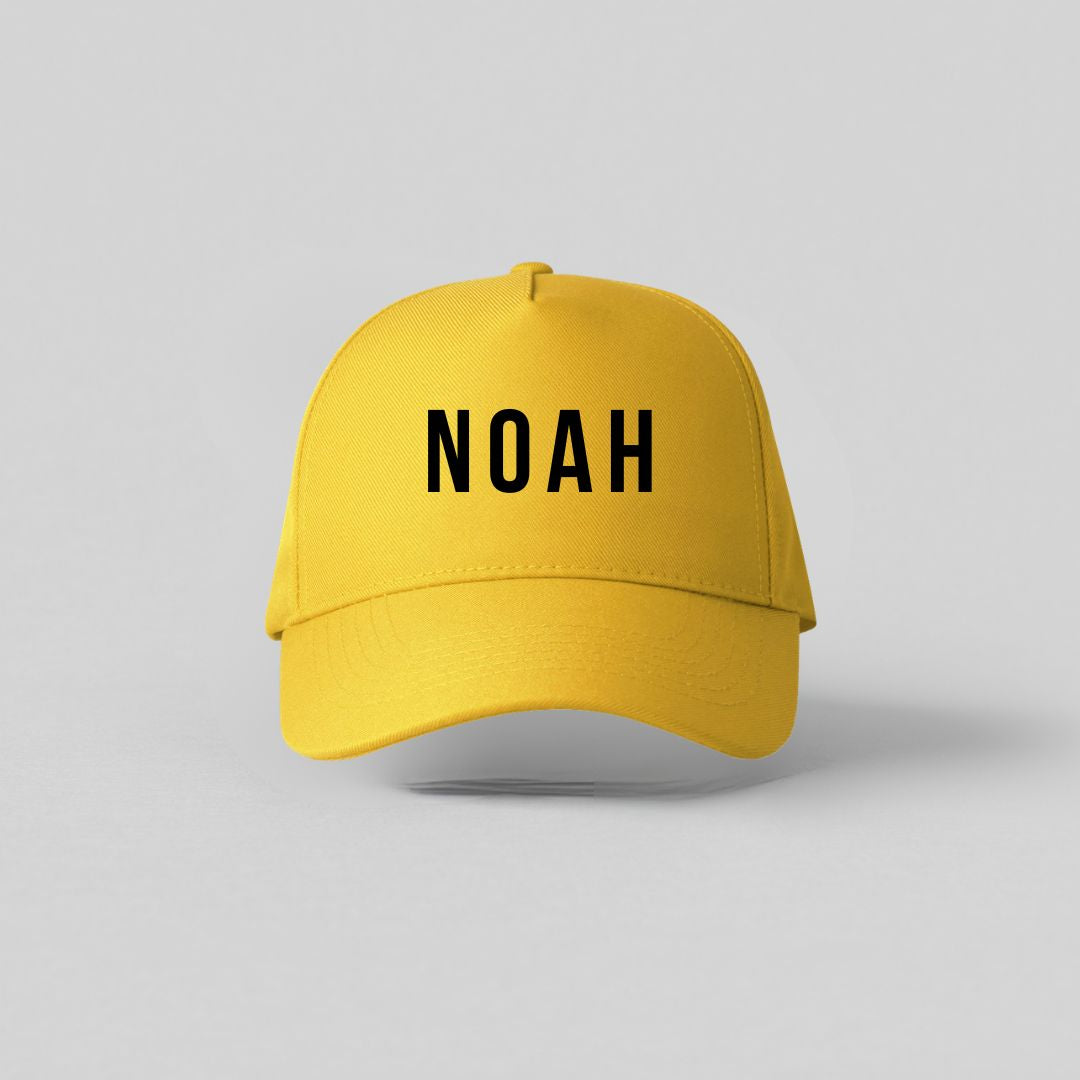 Gul børnekasket med sort navnetryk Noah set forfra